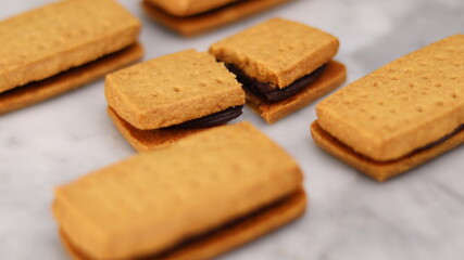 A close-up of handmade chocolate sandwich cookies tied with rustic twine, neatly stacked on a wooden plate. The golden brown biscuits with rich chocolate filling evoke a warm, homemade feel. Styled in