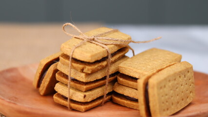 A close-up of handmade chocolate sandwich cookies tied with rustic twine, neatly stacked on a wooden plate. The golden brown biscuits with rich chocolate filling evoke a warm, homemade feel. Styled in