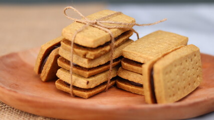 A close-up of handmade chocolate sandwich cookies tied with rustic twine, neatly stacked on a wooden plate. The golden brown biscuits with rich chocolate filling evoke a warm, homemade feel. Styled in