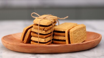 A close-up of handmade chocolate sandwich cookies tied with rustic twine, neatly stacked on a wooden plate. The golden brown biscuits with rich chocolate filling evoke a warm, homemade feel. Styled in