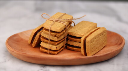 A close-up of handmade chocolate sandwich cookies tied with rustic twine, neatly stacked on a wooden plate. The golden brown biscuits with rich chocolate filling evoke a warm, homemade feel. Styled in