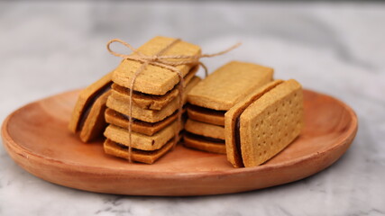 A close-up of handmade chocolate sandwich cookies tied with rustic twine, neatly stacked on a wooden plate. The golden brown biscuits with rich chocolate filling evoke a warm, homemade feel. Styled in