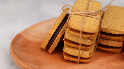 A close-up of handmade chocolate sandwich cookies tied with rustic twine, neatly stacked on a wooden plate. The golden brown biscuits with rich chocolate filling evoke a warm, homemade feel. Styled in