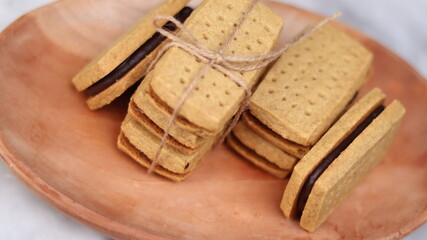 A close-up of handmade chocolate sandwich cookies tied with rustic twine, neatly stacked on a wooden plate. The golden brown biscuits with rich chocolate filling evoke a warm, homemade feel. Styled in