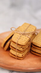 A close-up of handmade chocolate sandwich cookies tied with rustic twine, neatly stacked on a wooden plate. The golden brown biscuits with rich chocolate filling evoke a warm, homemade feel. Styled in