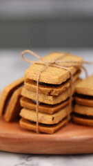 A close-up of handmade chocolate sandwich cookies tied with rustic twine, neatly stacked on a wooden plate. The golden brown biscuits with rich chocolate filling evoke a warm, homemade feel. Styled in