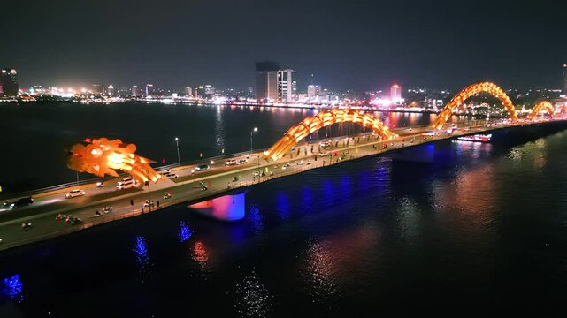 Dragon bridge illuminating nighttime da nang skyline, breathing fiery light as vehicles traverse metallic spine connecting urban landscape with dramatic architectural brilliance