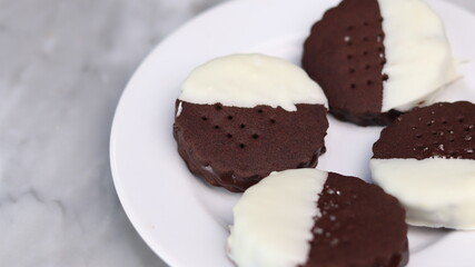 Delicious homemade chocolate ice cream sandwich cookies half dipped in white chocolate, served on a white plate over a marble background. A perfect frozen dessert or sweet treat for summer