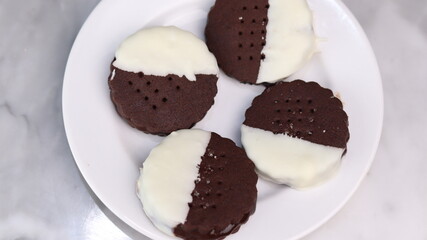 Delicious homemade chocolate ice cream sandwich cookies half dipped in white chocolate, served on a white plate over a marble background. A perfect frozen dessert or sweet treat for summer