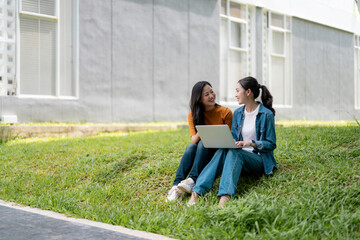 Two female students working on a laptop while sitting on grass in a university campus