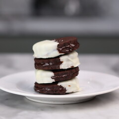 Delicious homemade chocolate ice cream sandwich cookies half dipped in white chocolate, served on a white plate over a marble background. A perfect frozen dessert or sweet treat for summer