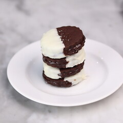 Delicious homemade chocolate ice cream sandwich cookies half dipped in white chocolate, served on a white plate over a marble background. A perfect frozen dessert or sweet treat for summer