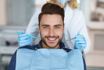 Smiling young bearded man sitting in dental chair, visiting modern dental clinic, having regular...