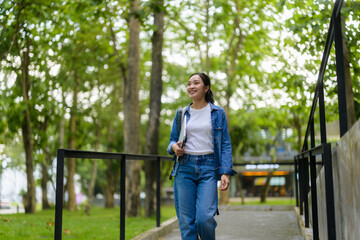 Young woman smiling and walking outdoors in a college campus with trees and grass, carrying a laptop and a backpack