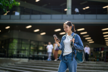 Young woman with backpack using mobile phone app in university campus