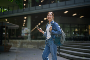 Asian female student using mobile phone and carrying backpack walking on university campus