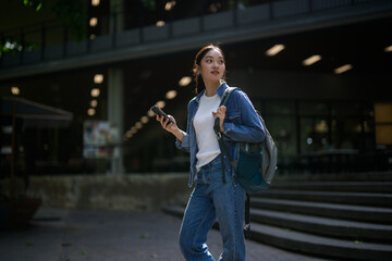 University student holding her smartphone while walking outside university campus building