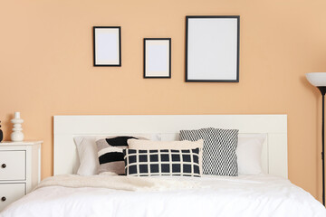 Big bed and blank frames on beige wall in room