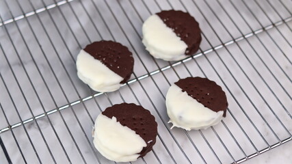 Chocolate ice cream sandwich cookies half dipped in white chocolate, arranged on a wire cooling rack over a marble surface. A clean and minimalistic composition showcasing frozen homemade desserts