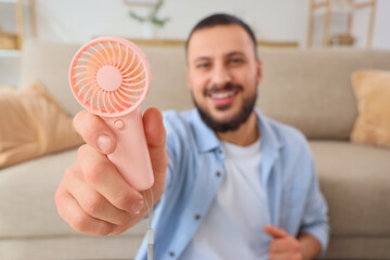 Young man with mini fan at home, closeup