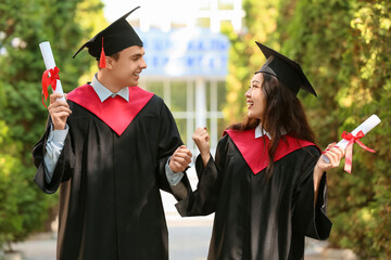 Couple of happy graduating students with diplomas outdoors