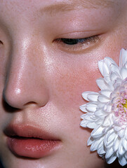 Soft natural beauty close up of a young woman with clear skin and closed eyes surrounded by white orchid flower for skincare and wellness concept