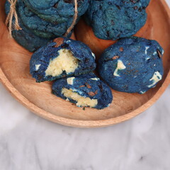 Vibrant blue chocolate chip cookies stacked and bundled with twine, served on a round wooden plate over a marble background. Eye-catching artisanal cookies perfect for bakery showcases, creative desse