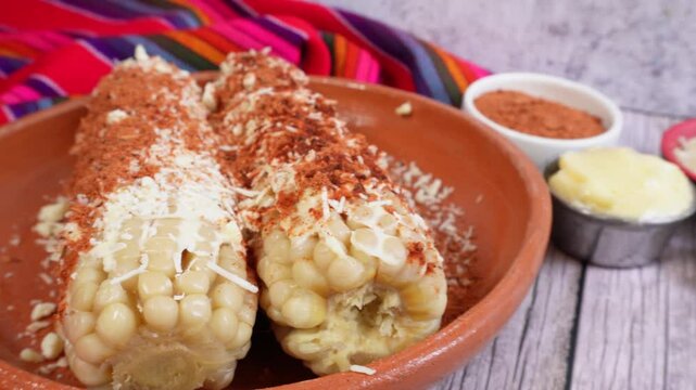 Travel to a pair of corn cobs prepared on a plate, near ingredients to prepare them, Mexican food