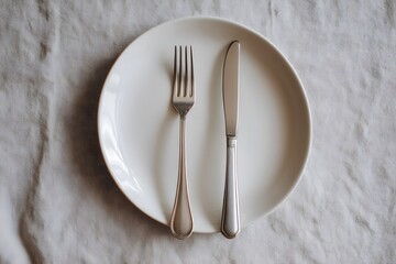 A minimalist setting featuring a white plate with a silver fork and knife placed on a light-colored tablecloth