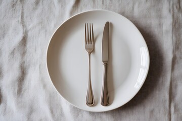 A minimalist dining setup featuring a white plate with a silver fork and knife placed on a light-colored tablecloth