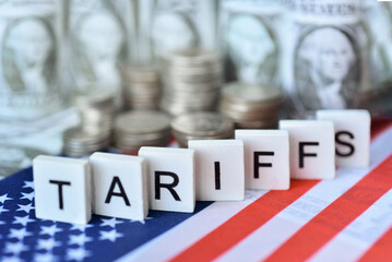 " Tariffs" wooden word on US flag with US dolla bills . US new import taxes announced by Donal Trump. Affected to baseline tariff, reciprocal tariffs, deminimis rule impack on global economy