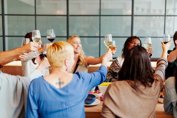 Group of diverse people raising glasses in celebration. Mixed gender and ethnicity. Smiling faces, joyful atmosphere, and toasting in a lively gathering. People in festive dinner, celebration.