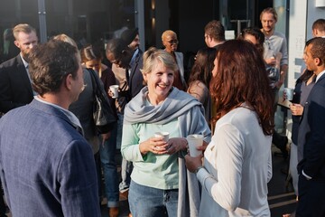 Group of diverse adults socializing outdoors, holding coffee cups. Casual gathering with men and...