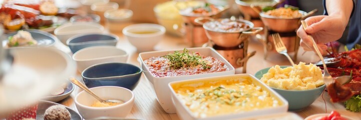 A buffet table with various dishes, including mashed potatoes, sauces, and garnishes. A hand serves food from the buffet, showcasing a variety of colorful dishes. Buffet table with delicious food.