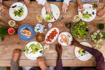 Top view of diverse group enjoy healthy meal, salad and salmon. Diverse people hands reach for food...
