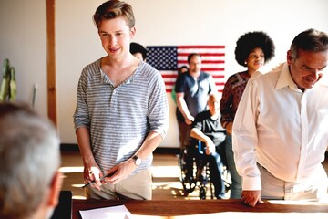 US election day,  Diverse people wait in line to vote at US election station with American flag in...