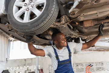 Automotive Mechanic Inspecting Undercarriage of Car, Professional Technician Working on Vehicle Lift, Smiling Mechanic Performing Car Service