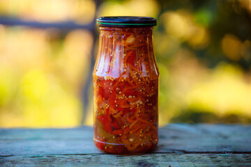 Home preservation. Vegetable salad in a glass jar on a wooden table. Natural green background with smooth bokeh. Healthy food concept. Vegetables from the garden.