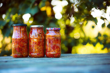 Home preservation. Vegetable salad in a glass jar on a wooden table. Natural green background with...