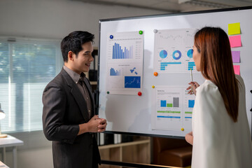 A man and a woman are standing in front of a white board with graphs and charts