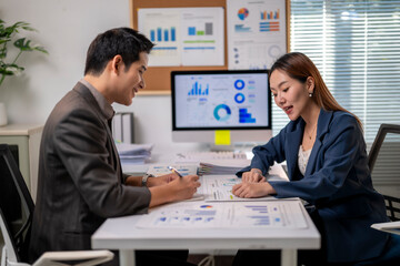 Two people are sitting at a desk with a computer monitor in front of them