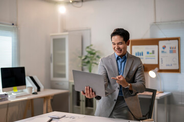 A man in a suit is smiling and pointing at a laptop screen