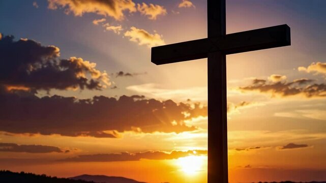 Silhouette of a wooden Christian cross against a colorful sunset sky with light clouds over a landscape. Symbol of faith and hope.