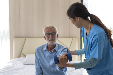 Elderly Caucasian man holding dumbbell exercise with female caregiver helping in senior home care