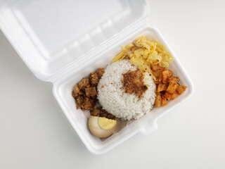 Steamed rice served with boiled egg, potato chip, fried tempeh in Styrofoam container