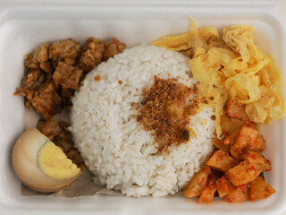Steamed rice served with boiled egg, potato chip, fried tempeh in Styrofoam container