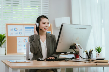 Smiling Asian female call center agent wearing a headset, speaking with a client at her office...
