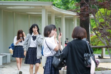 Obraz premium In early June in Pudong, Shanghai, four Japanese high school girls in summer uniforms gather in front of their school, chatting and smiling in the warm sun and breeze as they get ready for the day.