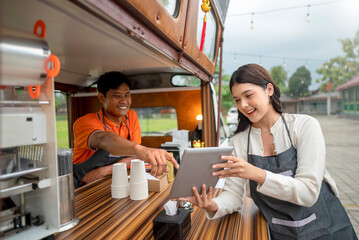 Indonesian southeast asian male with a Chinese female couple barista holding a tablet while discussing in their coffee shop. A small business of a coffee shop or cafe on a truck