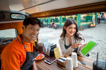 Indonesian southeast asian male with a Chinese female couple barista holding a tablet while discussing in their coffee shop. Mockup or copy space. A small business of a coffee shop or cafe on a truck
